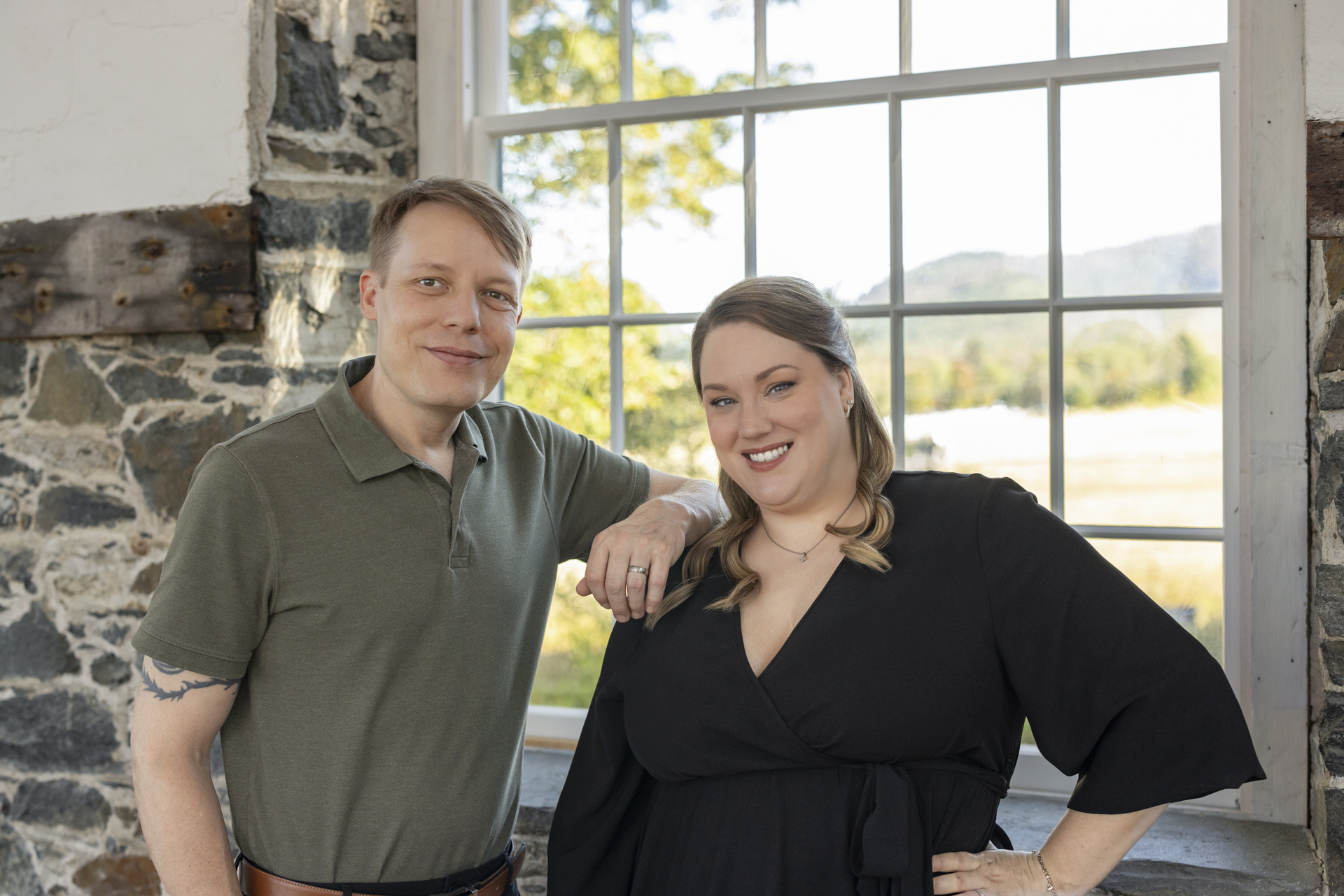 Ron and Alicia Hirte posing in front of a large window with trees and mountains visible outside