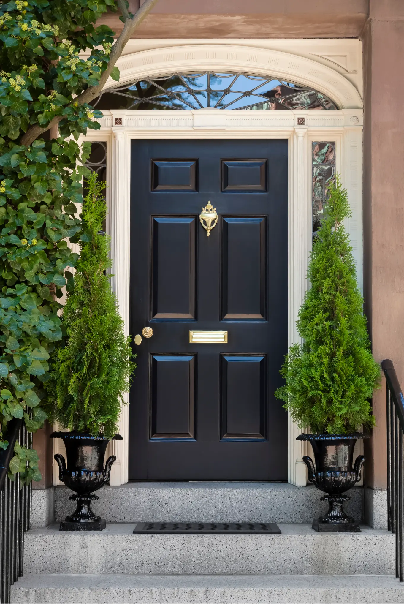 A beautiful front entryway with a black door surrounded by evergreen topiary